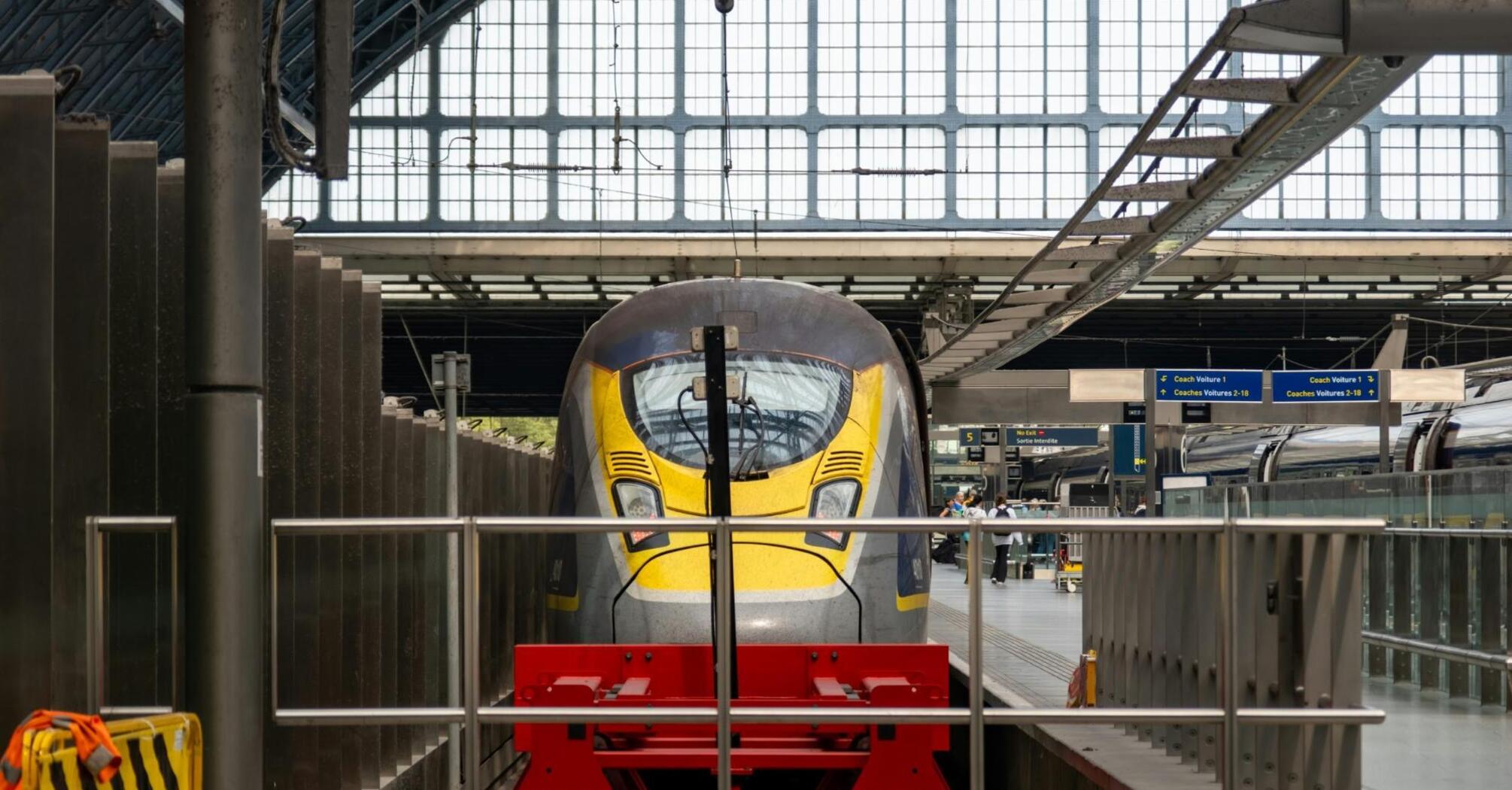 A modern train at a station platform inside a bright, glass-covered terminal