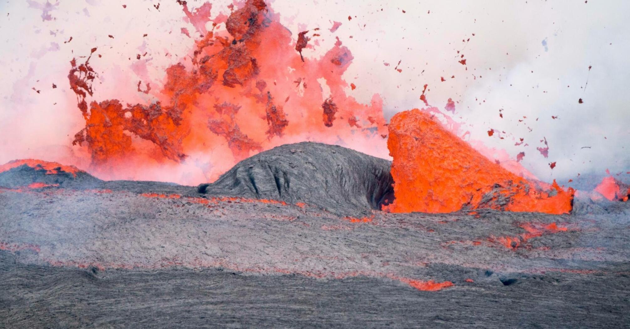 A vivid volcanic eruption with lava spewing and flowing over rugged terrain