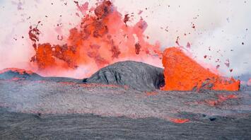 A vivid volcanic eruption with lava spewing and flowing over rugged terrain