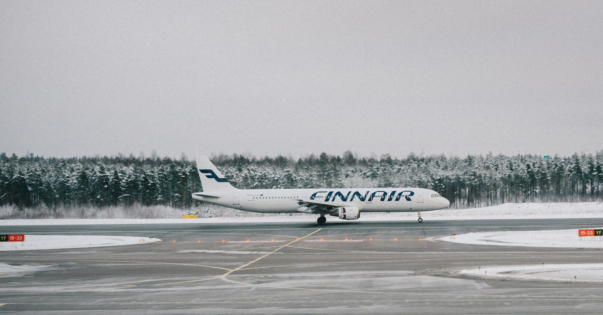 Finnair aircraft parked on a snowy runway surrounded by trees in winter