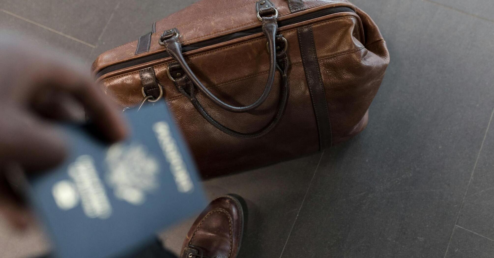 A brown leather travel bag and a passport in hand