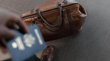 A brown leather travel bag and a passport in hand