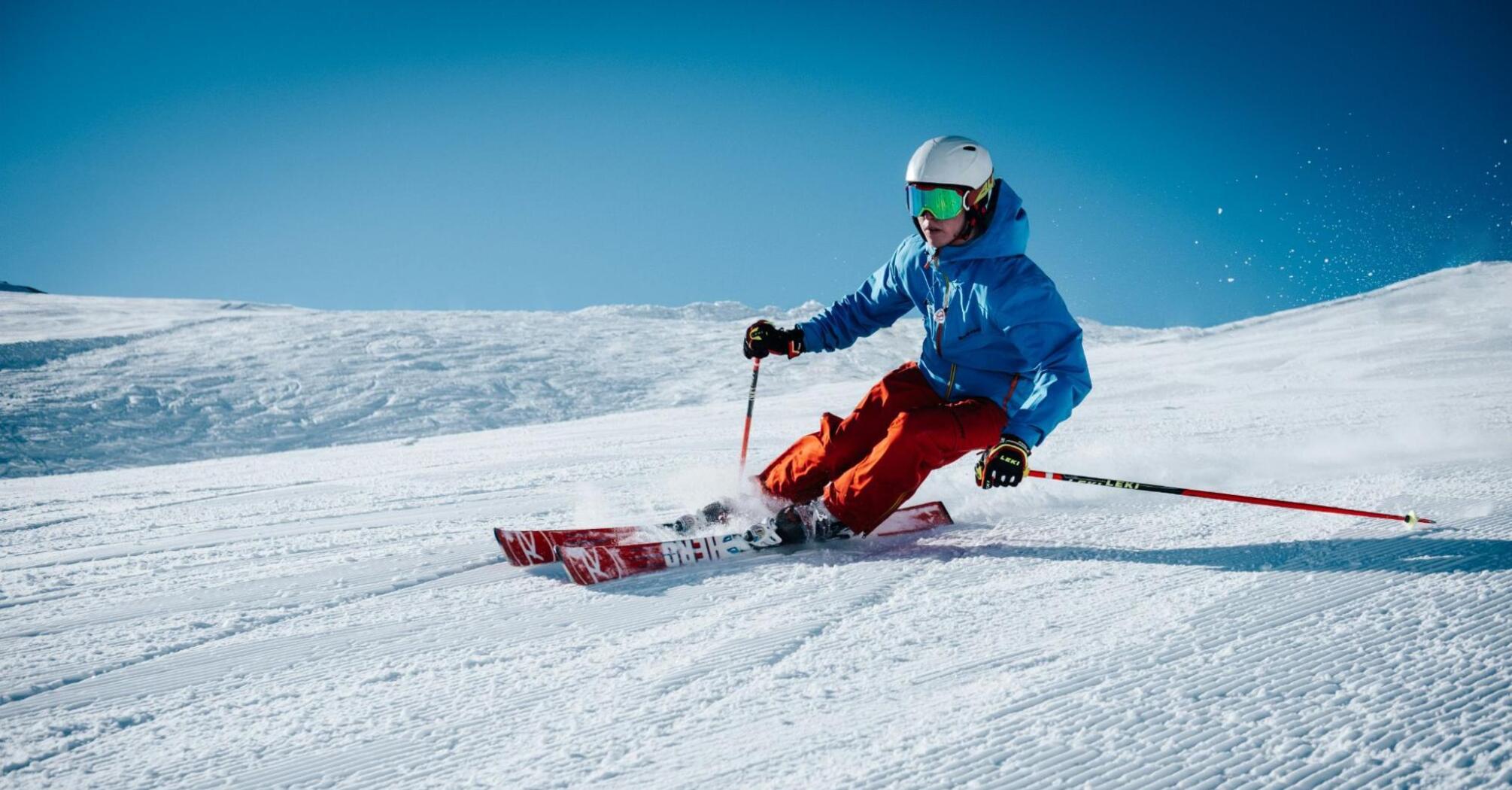 Skier carving down a pristine snowy slope on a clear sunny day