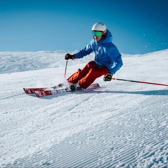 Skier carving down a pristine snowy slope on a clear sunny day