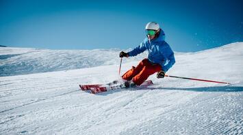 Skier carving down a pristine snowy slope on a clear sunny day