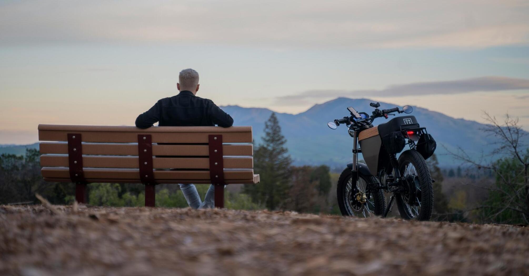 A person sitting on a bench beside an electric bike with a scenic mountain view in the background