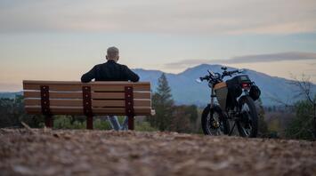 A person sitting on a bench beside an electric bike with a scenic mountain view in the background