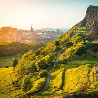 View of Edinburgh cityscape from Arthur's Seat, featuring a green hill and historic skyline at sunset