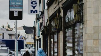 A person in a blue cloak walking near a bus stop labeled "Kings Theatre" in Portsmouth, with nearby shops visible