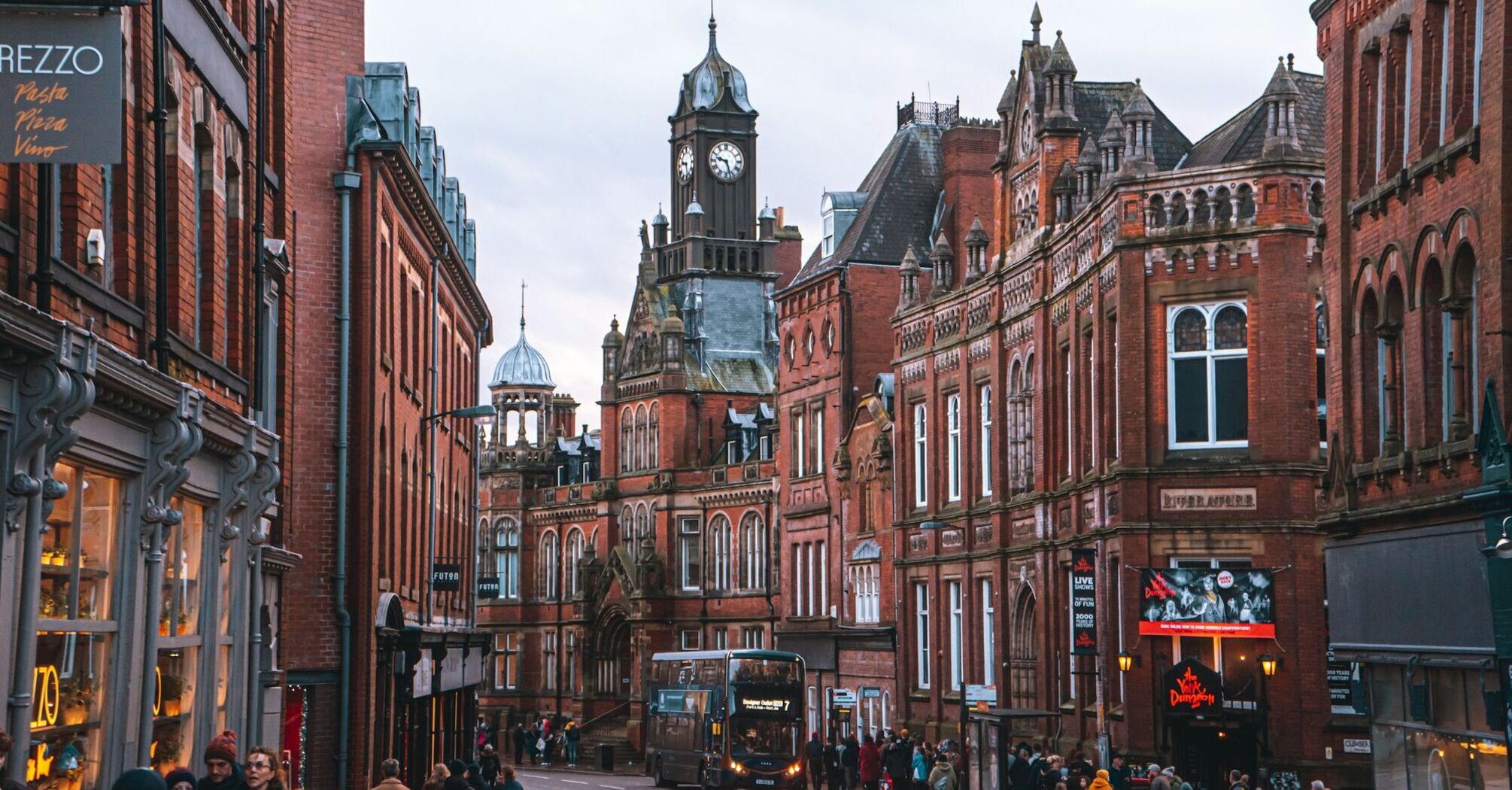 A bustling street in York with historic red-brick buildings and a clock tower in view, showcasing the city's charm