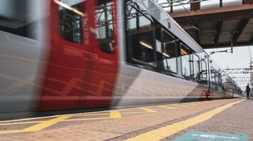 A modern train arriving at a station platform, with directional markings on the ground for passenger guidance