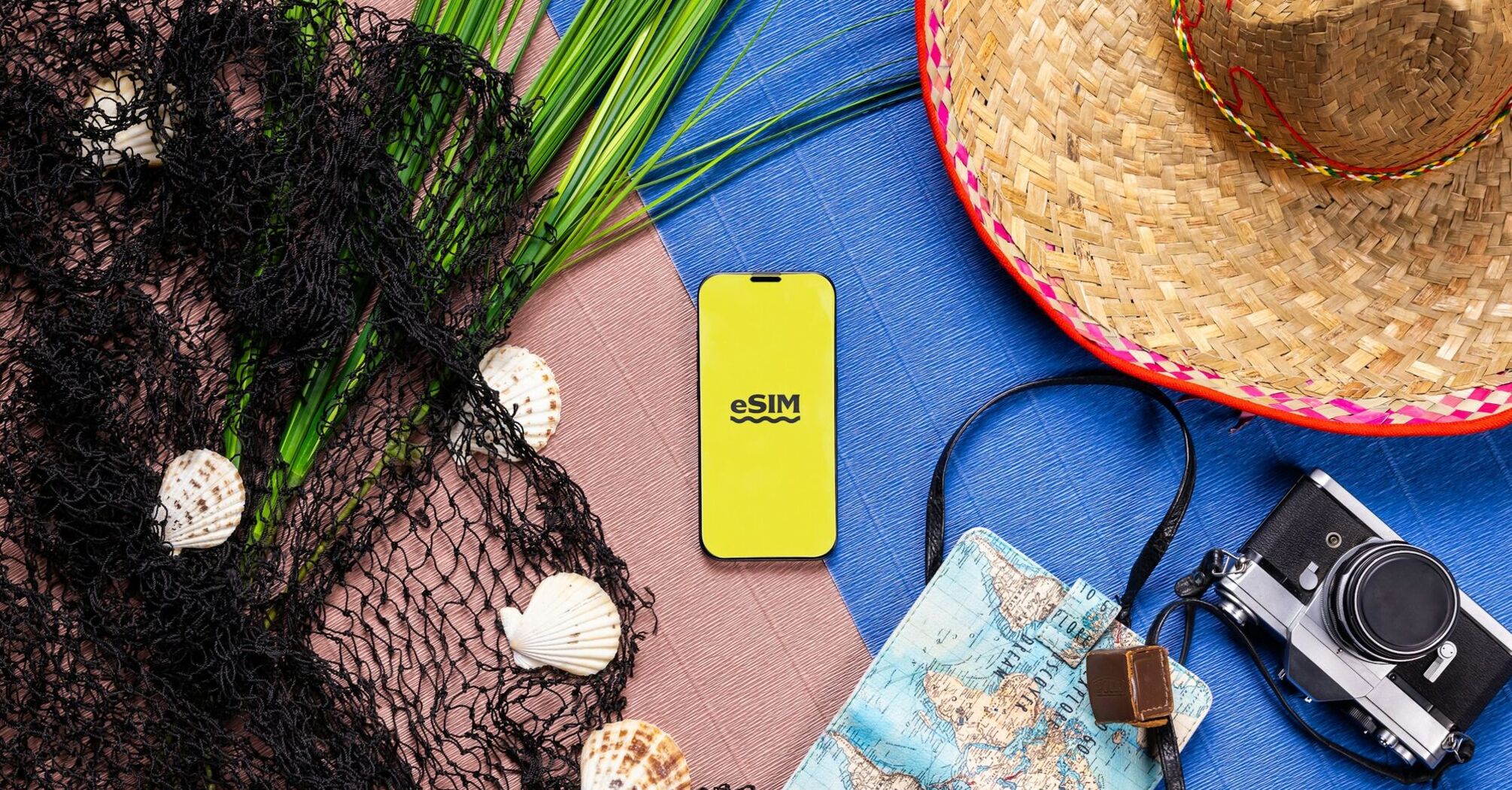 A smartphone displaying "eSIM" surrounded by travel accessories, including seashells, a map, a camera, and a straw hat, symbolizing travel readiness