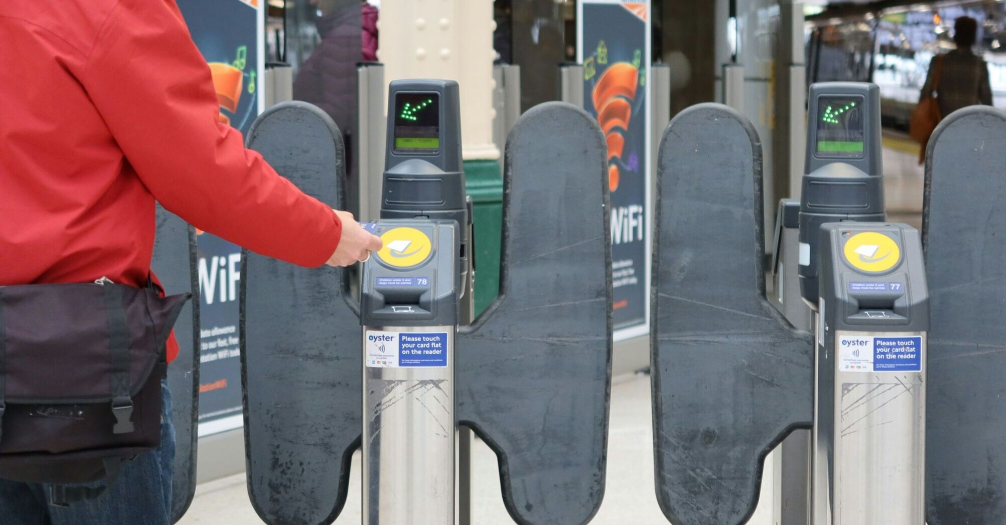 A passenger taps a contactless payment card at a rail station turnstile