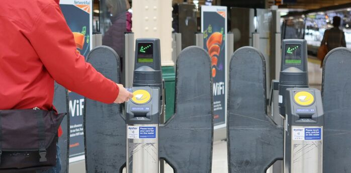 A passenger taps a contactless payment card at a rail station turnstile