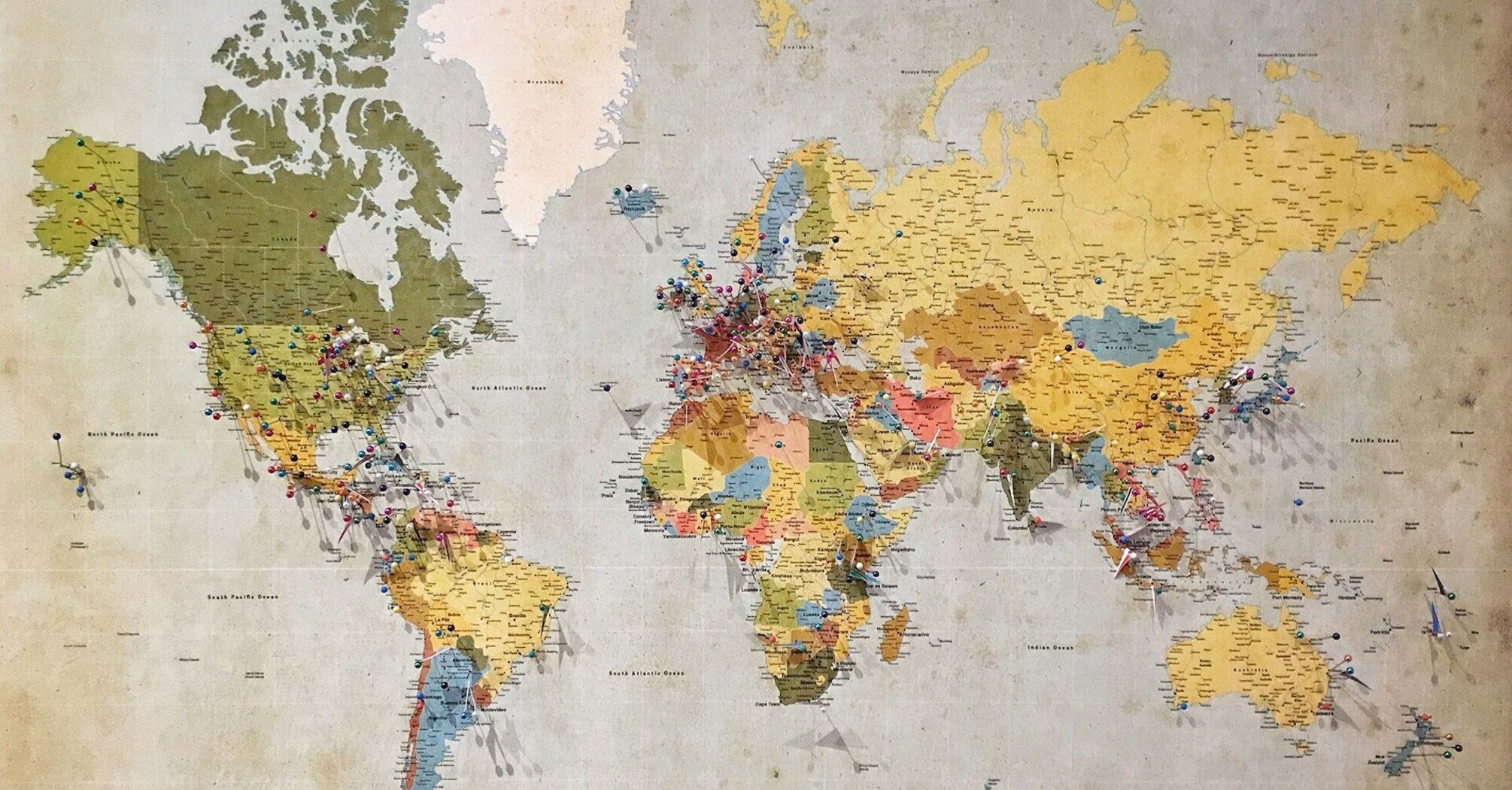 A vintage world map with colorful pins marking various global destinations