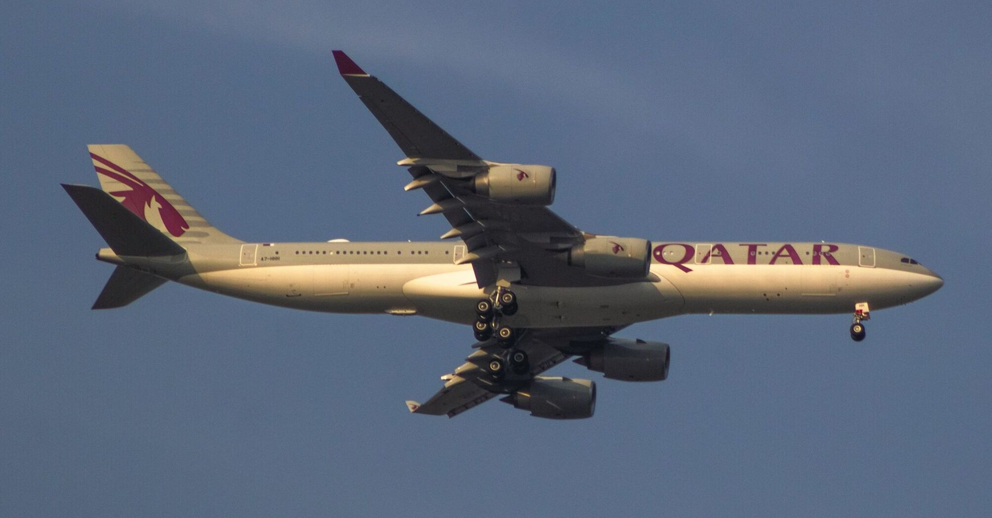 A Qatar Airways aircraft in flight with landing gear down against a clear sky