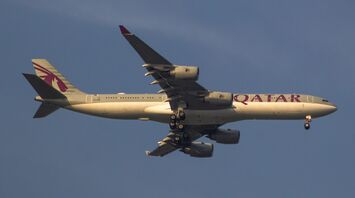 A Qatar Airways aircraft in flight with landing gear down against a clear sky