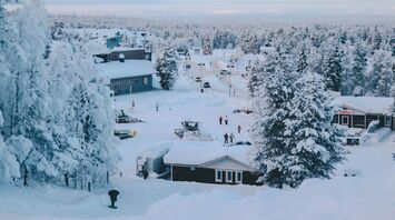 Snow-covered village in Finnish Lapland with trees, small buildings, and people walking through the winter landscape