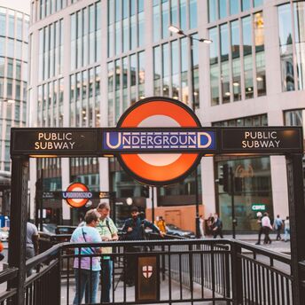 London Underground entrance with people and modern buildings in the background