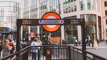 London Underground entrance with people and modern buildings in the background