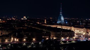 A nighttime view of Turin, Italy, featuring the illuminated Mole Antonelliana and surrounding cityscape