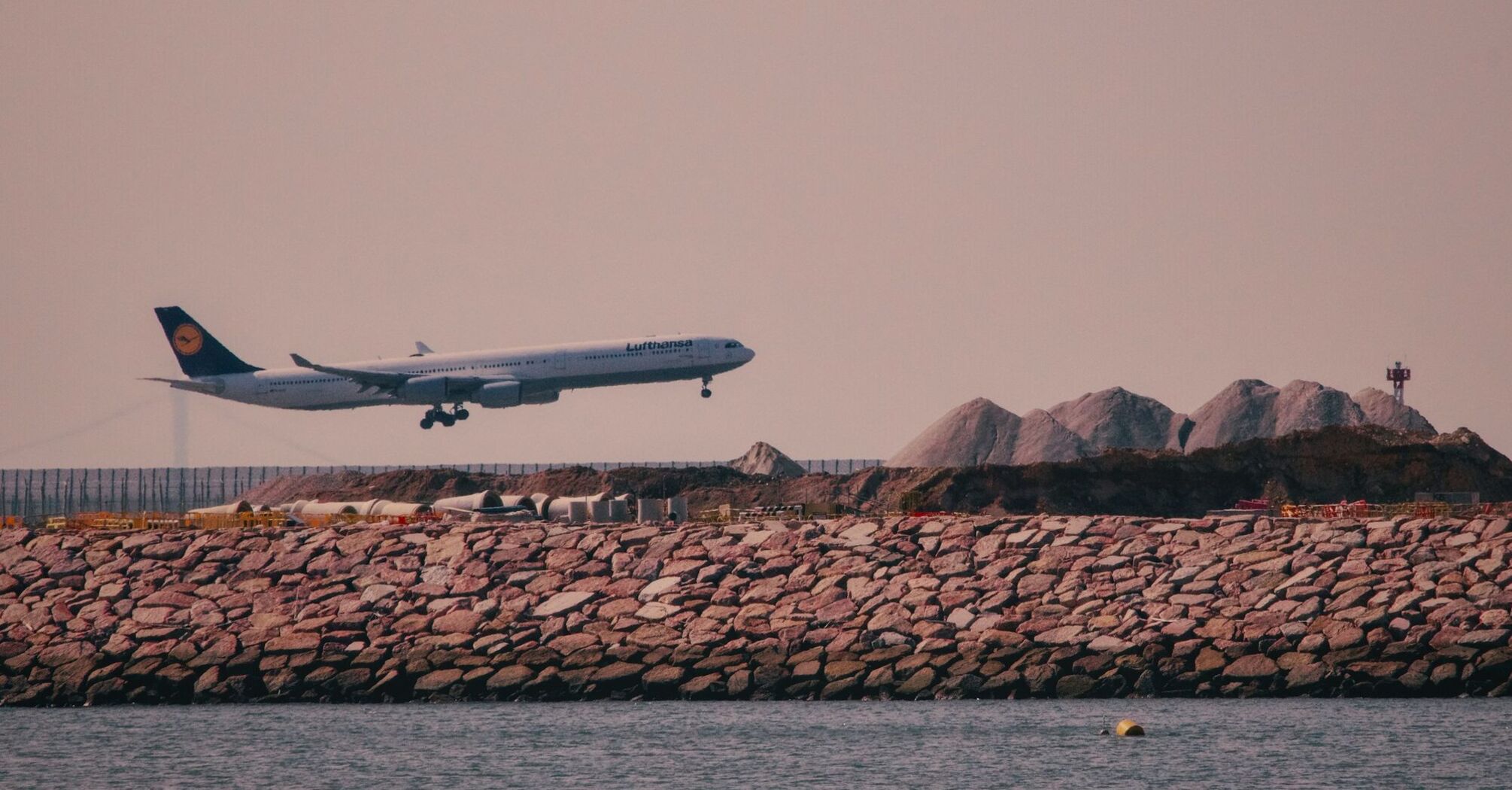 A Lufthansa airplane landing near a rocky coastline under a clear sky