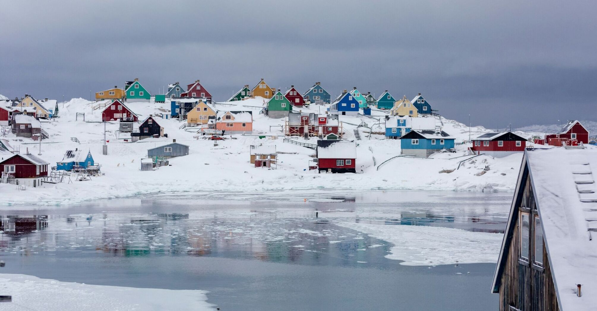 The town of Aasiaat in Greenland during winter, showcasing colorful houses on a snowy hillside near partially frozen waters