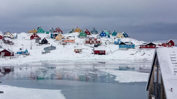The town of Aasiaat in Greenland during winter, showcasing colorful houses on a snowy hillside near partially frozen waters