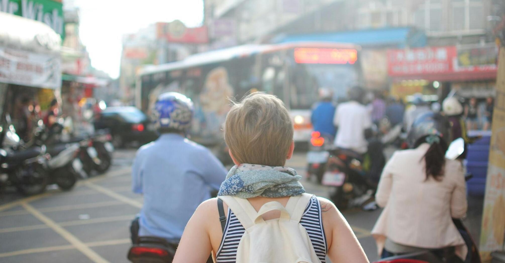 A backpacked tourist navigates a crowded urban street filled with motorbikes and vibrant signs