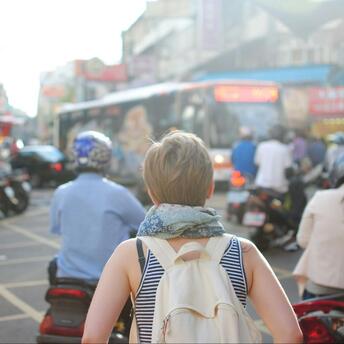 A backpacked tourist navigates a crowded urban street filled with motorbikes and vibrant signs