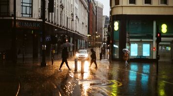 A rainy street in a UK city with people crossing the road under umbrellas, reflecting the unsettled weather