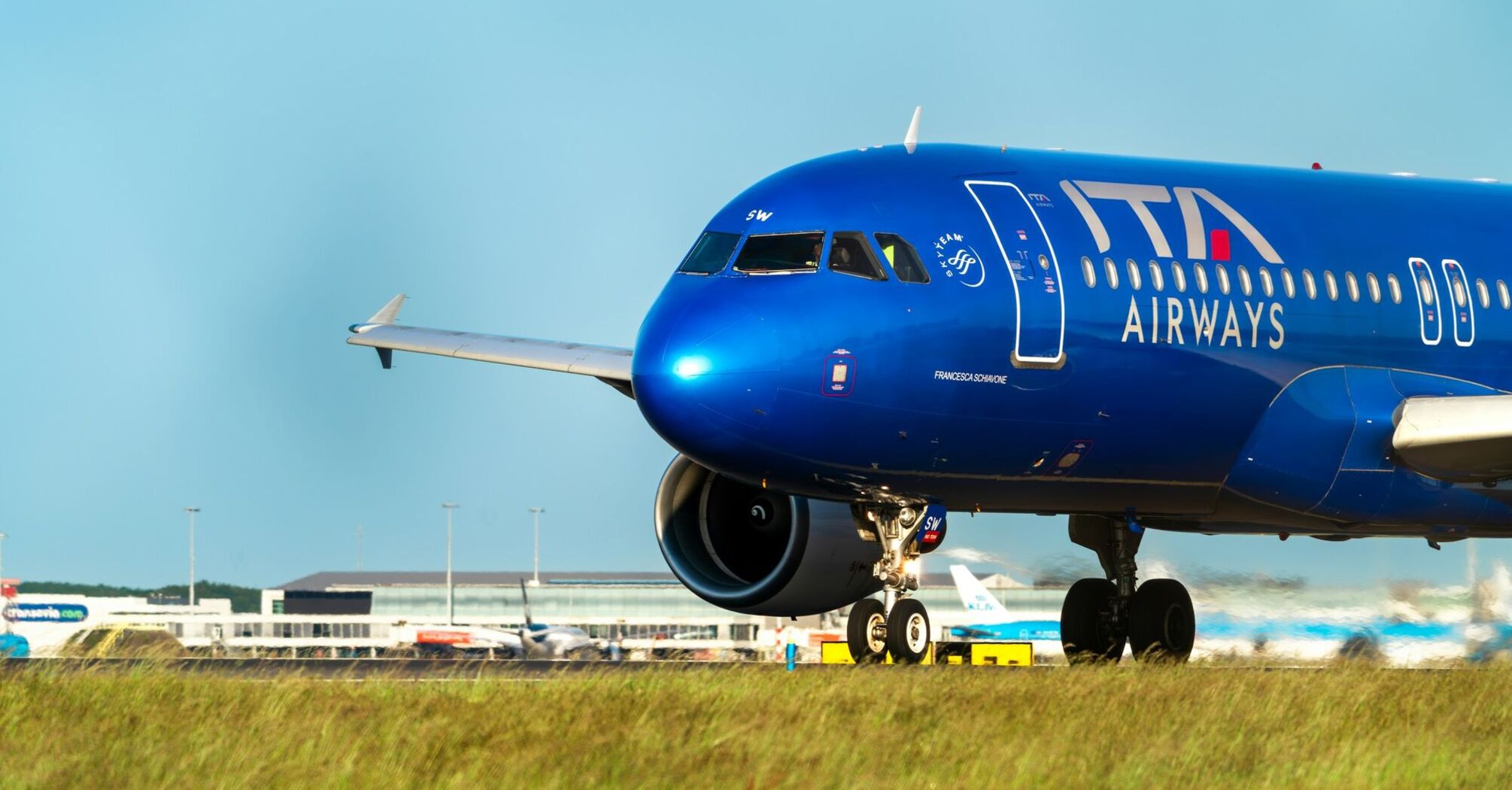 A blue ITA Airways plane on a runway under a clear sky