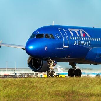 A blue ITA Airways plane on a runway under a clear sky