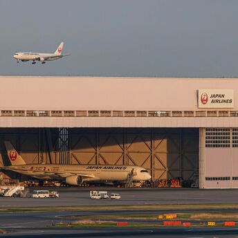 Japan Airlines planes near a hangar with one aircraft landing and another undergoing maintenance at Haneda Airport