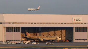 Japan Airlines planes near a hangar with one aircraft landing and another undergoing maintenance at Haneda Airport