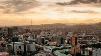 Aerial view of Ulaanbaatar, Mongolia's capital, with a blend of modern buildings and surrounding hills under a golden sunset sky