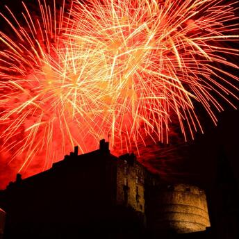 Bright red fireworks illuminating the night sky above Edinburgh Castle
