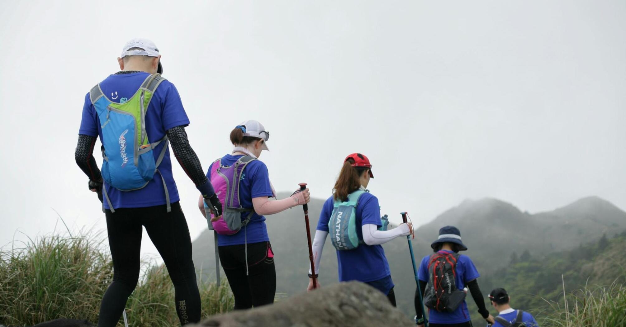 A group of hikers walking along a mountain trail, wearing backpacks and using trekking poles, with misty mountains in the background