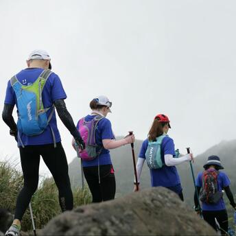 A group of hikers walking along a mountain trail, wearing backpacks and using trekking poles, with misty mountains in the background