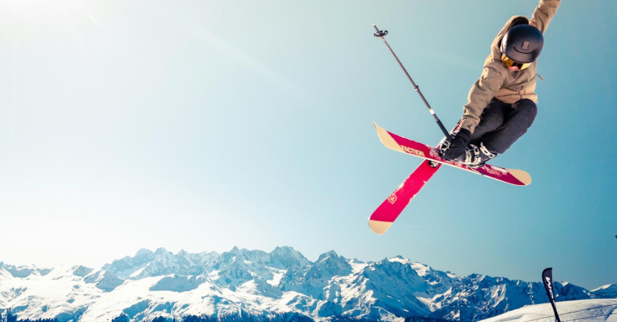 Skier performing a high jump on snowy mountains under clear sky