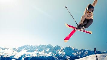 Skier performing a high jump on snowy mountains under clear sky