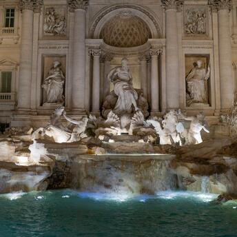The Trevi Fountain in Rome illuminated at night, showcasing its intricate Baroque sculptures