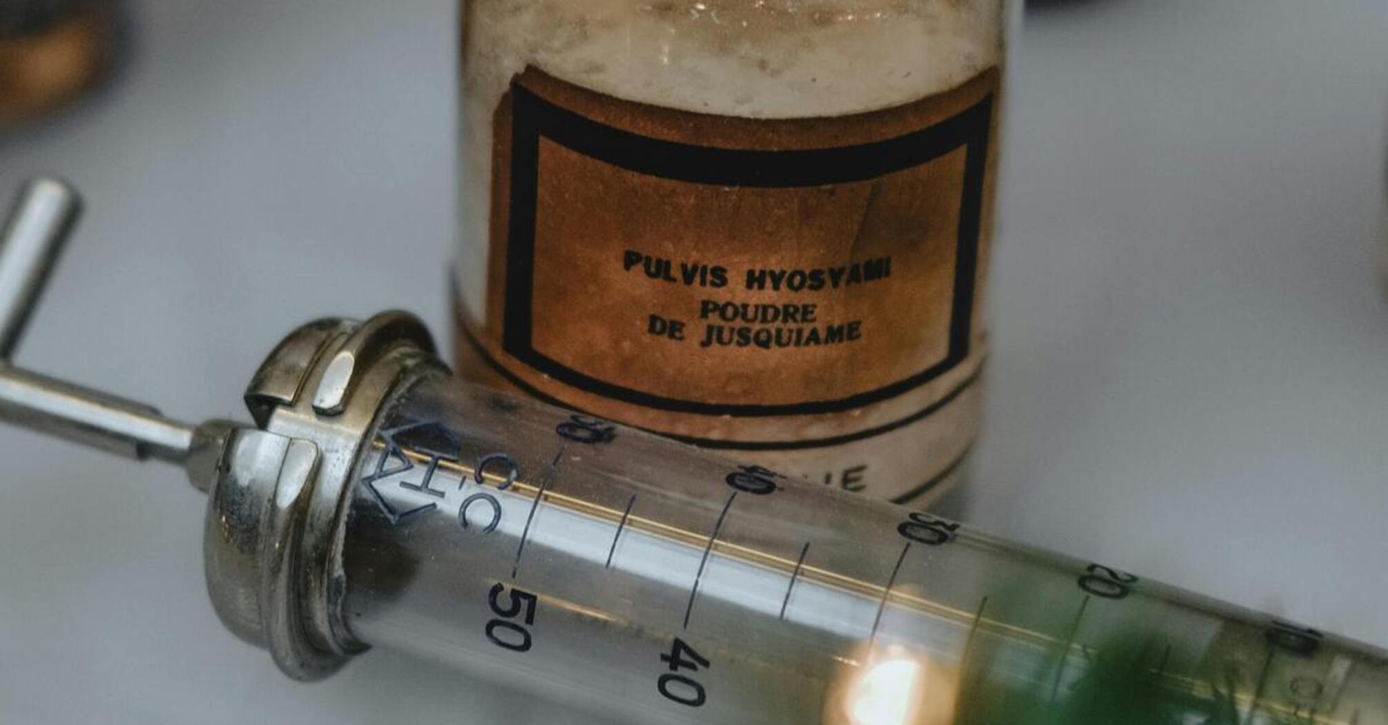 Vintage medical bottle labeled 'Pulvis Hyoscyami' and a metal syringe