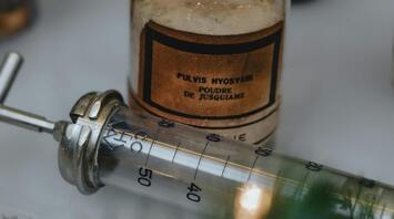 Vintage medical bottle labeled 'Pulvis Hyoscyami' and a metal syringe
