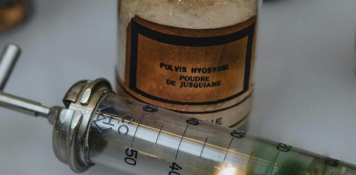 Vintage medical bottle labeled 'Pulvis Hyoscyami' and a metal syringe
