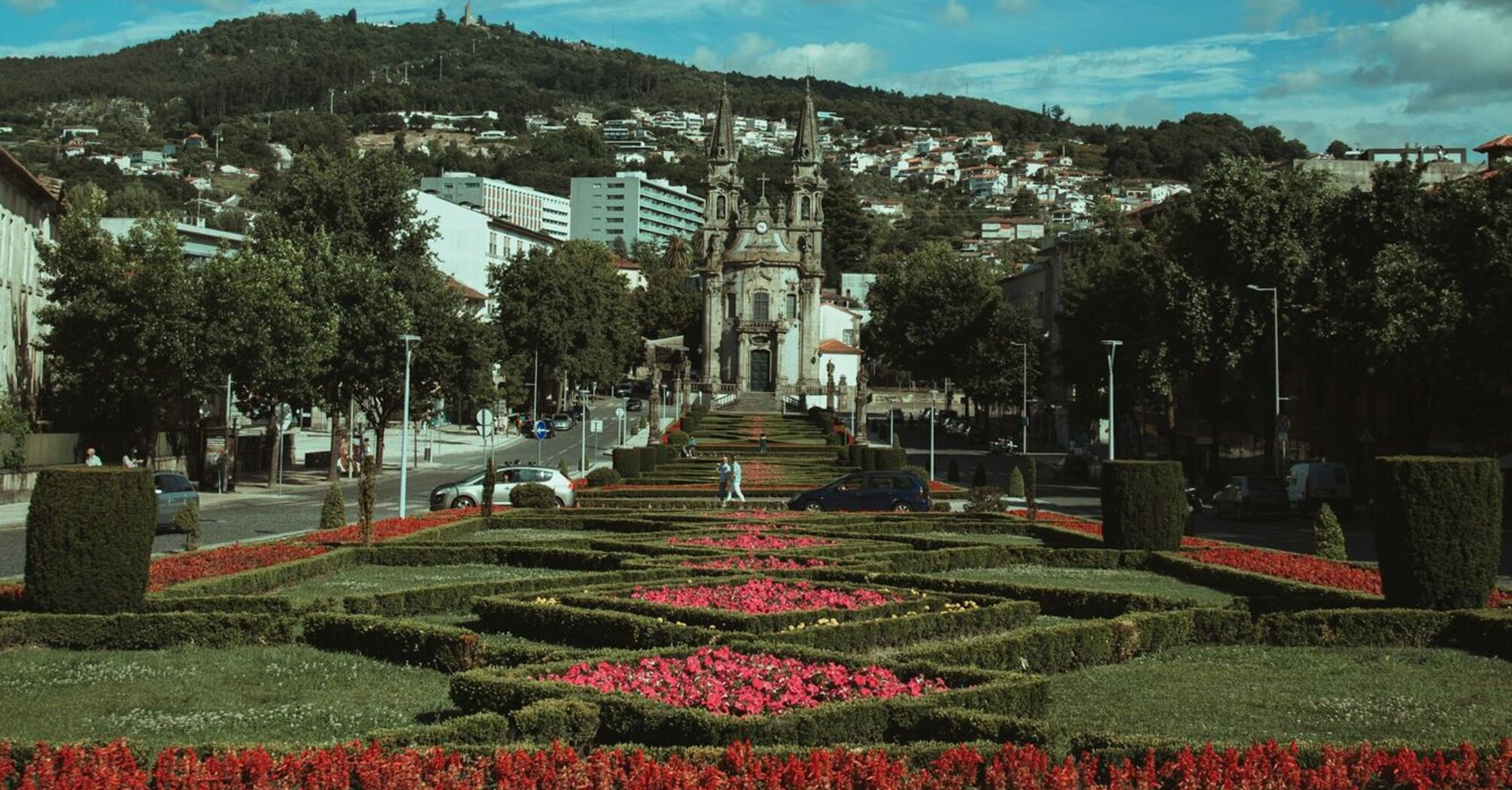 A scenic view of Guimarães, Portugal, featuring a historic church surrounded by manicured gardens under a vibrant sky