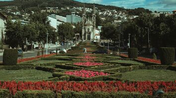 A scenic view of Guimarães, Portugal, featuring a historic church surrounded by manicured gardens under a vibrant sky