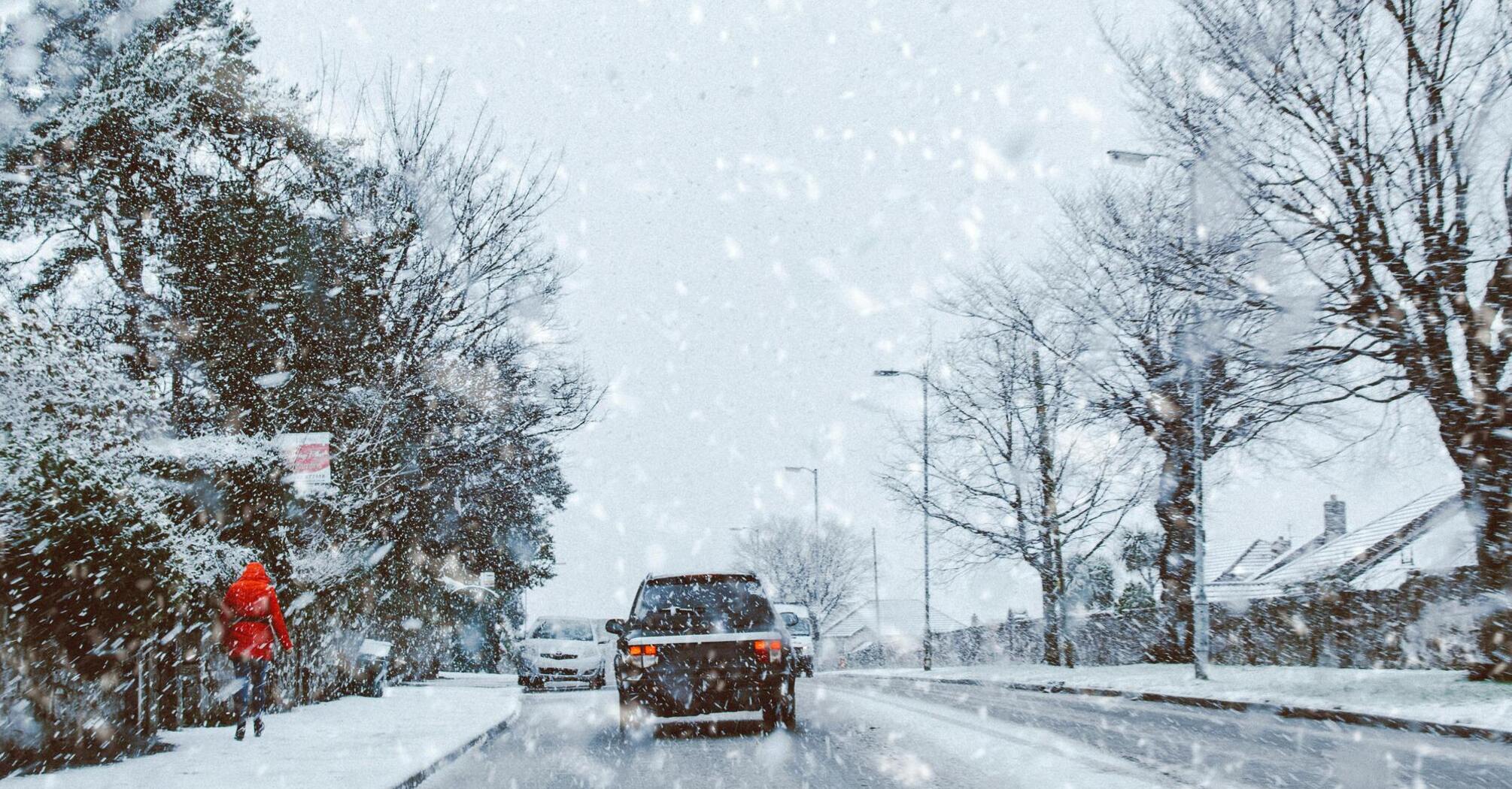 Snow-covered street with cars and pedestrians during heavy snowfall