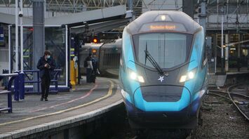 A TransPennine Express train at a station platform with passengers nearby, displaying "Manchester Airport" on its destination board
