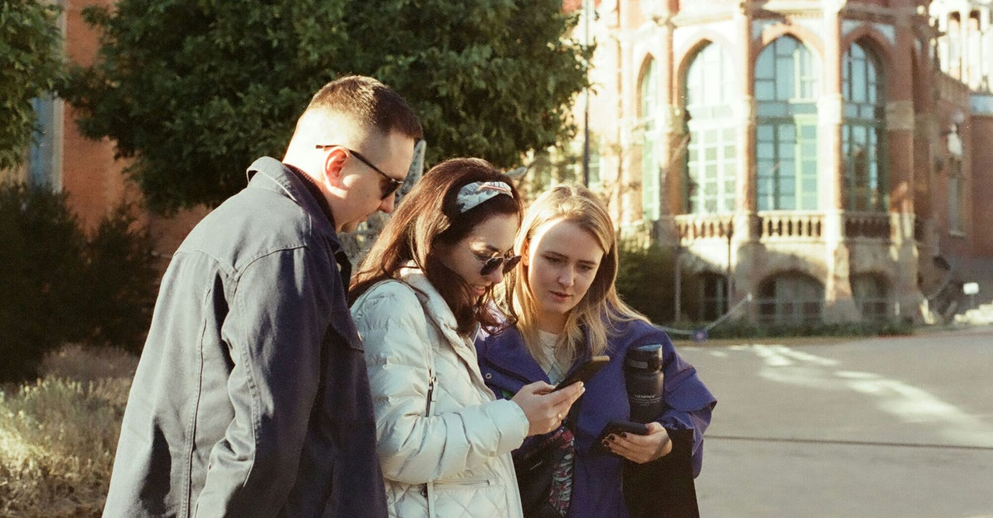 Three people looking at a smartphone outside a historic building